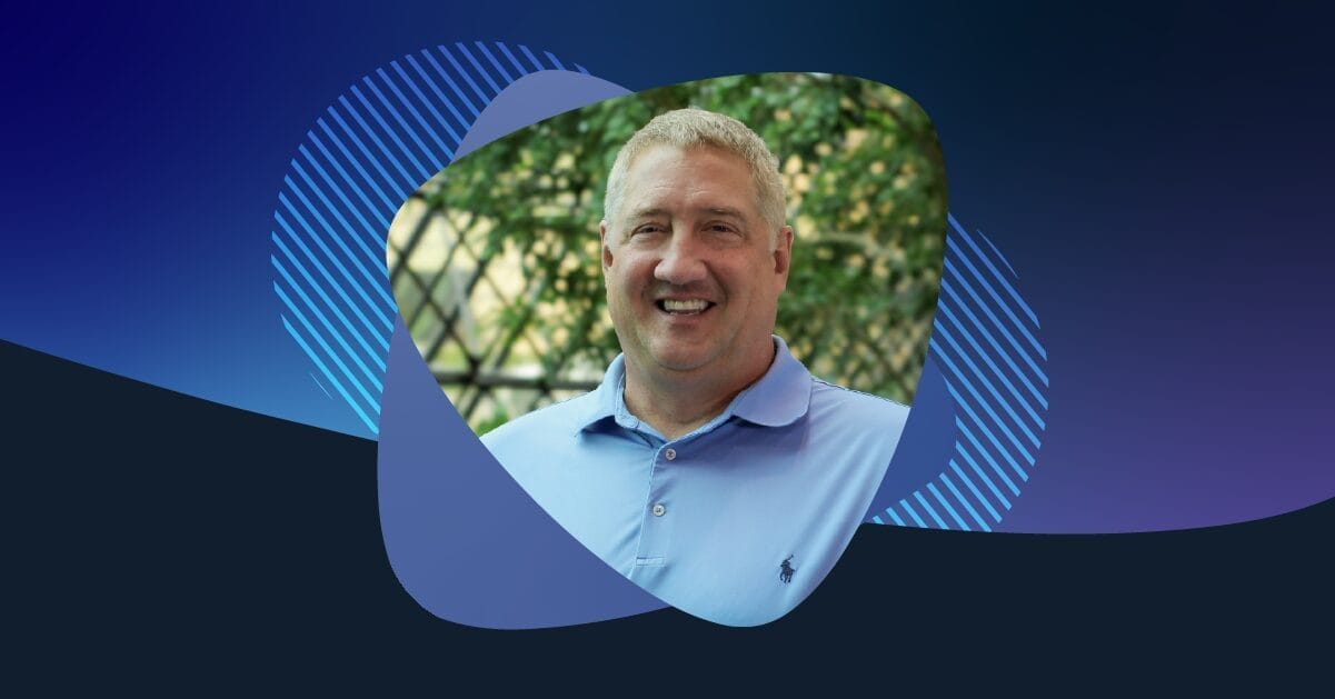 John Bissa, smiling in a light blue polo shirt, stands outdoors with trees in the background and a modern Apex Digital graphic frame.
